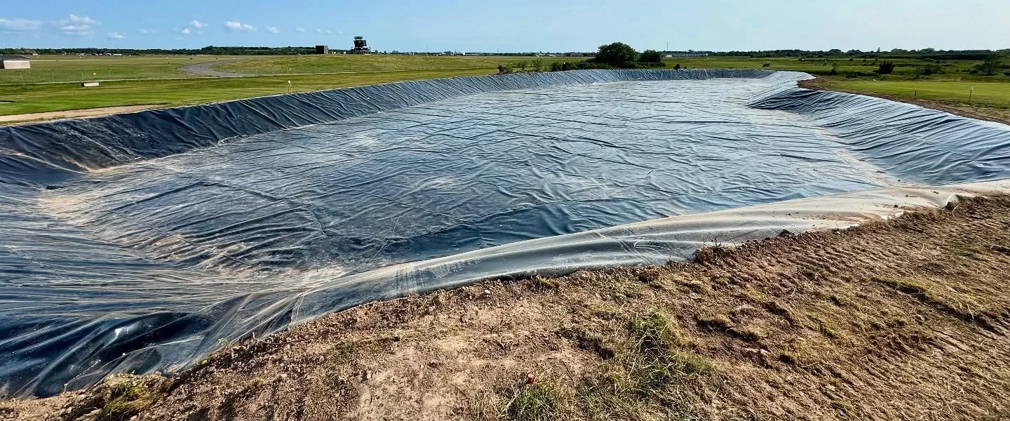 Bevattningsdamm under anläggning med utlagd geomembran i ett öppet fält